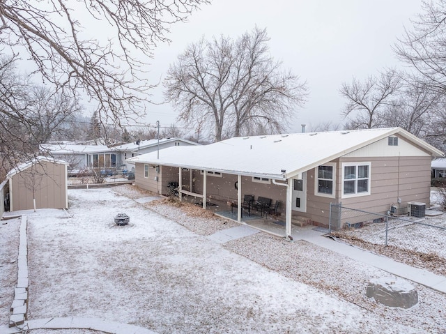 snow covered back of property featuring a storage unit, central AC, and an outdoor fire pit