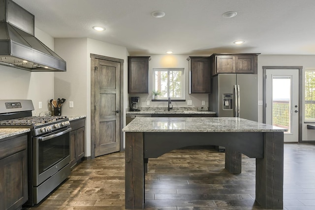 kitchen with light stone countertops, sink, wall chimney exhaust hood, dark wood-type flooring, and stainless steel appliances