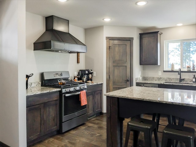 kitchen featuring dark hardwood / wood-style flooring, light stone counters, stainless steel gas range oven, sink, and wall chimney range hood