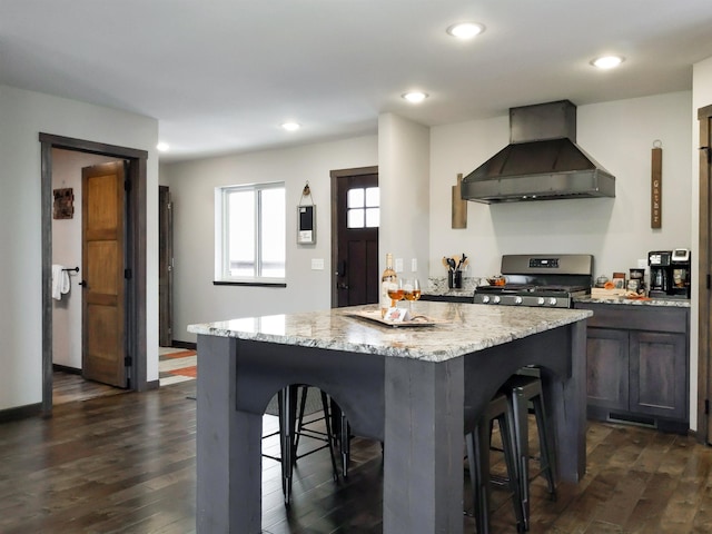 kitchen featuring wall chimney exhaust hood, light stone counters, a breakfast bar area, and gas range