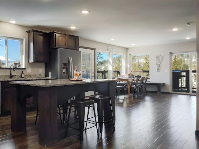 kitchen with stainless steel fridge, a kitchen island, dark brown cabinets, and light stone counters