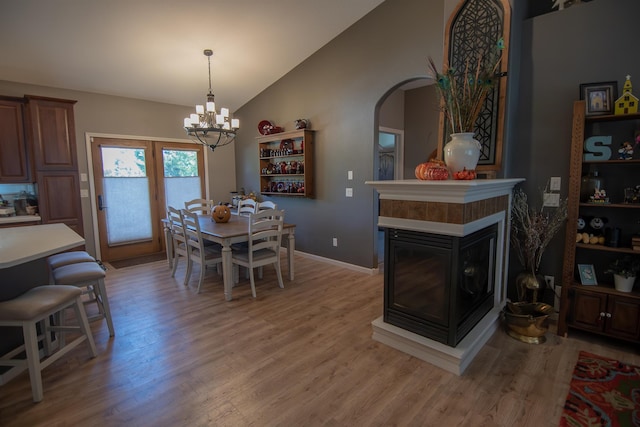 dining room with a multi sided fireplace, hardwood / wood-style flooring, vaulted ceiling, and a notable chandelier