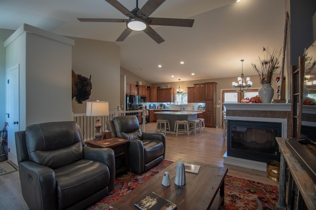 living room with ceiling fan with notable chandelier, light hardwood / wood-style floors, and lofted ceiling