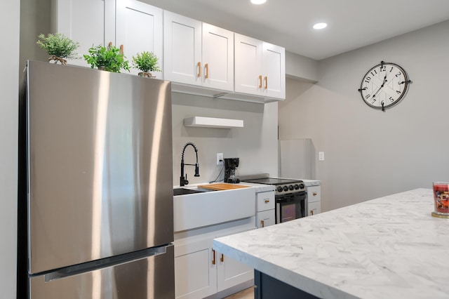 kitchen with white cabinetry, stainless steel fridge, electric range, and light stone countertops