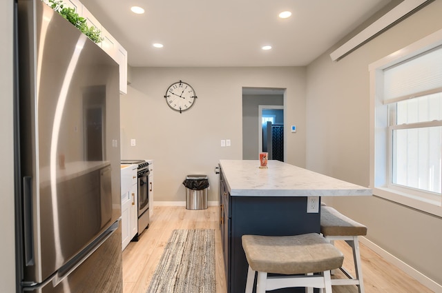 kitchen featuring a kitchen bar, appliances with stainless steel finishes, a center island, light hardwood / wood-style floors, and white cabinetry