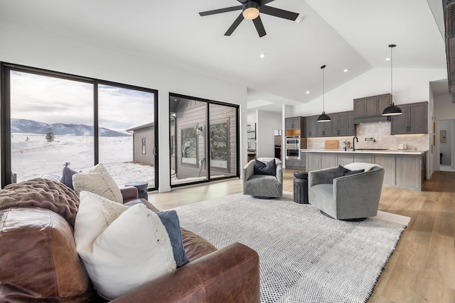 living room featuring high vaulted ceiling, sink, ceiling fan, a mountain view, and light hardwood / wood-style flooring