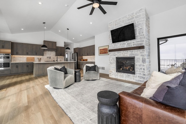 living room with ceiling fan, sink, light hardwood / wood-style flooring, high vaulted ceiling, and a fireplace