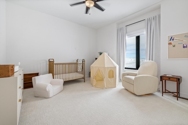 carpeted bedroom with a crib and ceiling fan