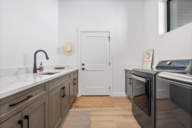 laundry area featuring cabinets, separate washer and dryer, sink, and light wood-type flooring