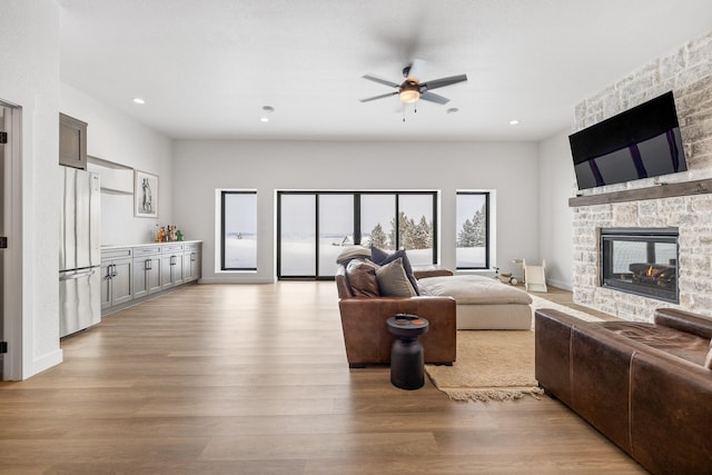 living room with ceiling fan, a stone fireplace, and light wood-type flooring