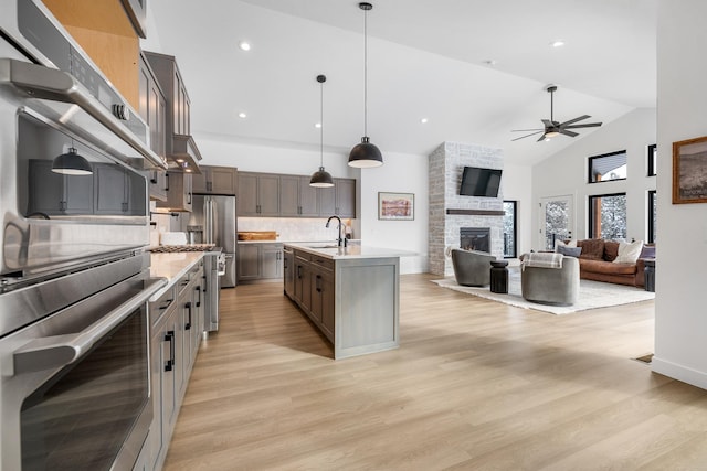 kitchen with sink, a center island with sink, pendant lighting, stainless steel appliances, and a fireplace