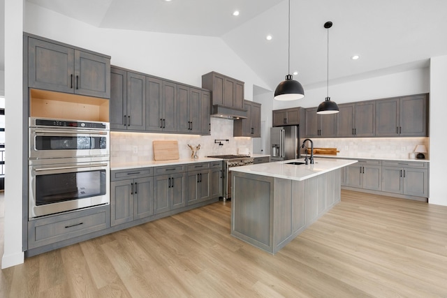 kitchen featuring pendant lighting, high quality appliances, sink, light hardwood / wood-style floors, and a center island with sink