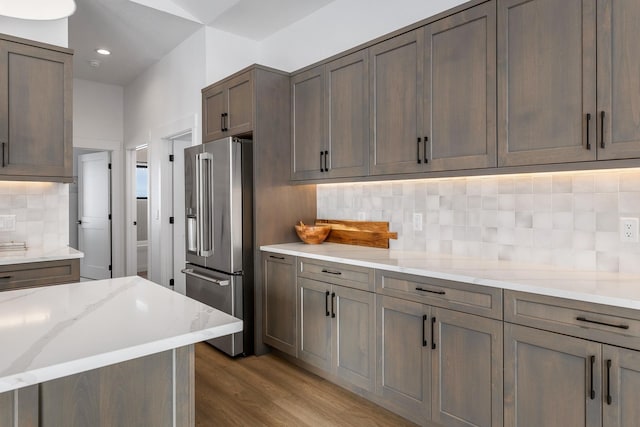 kitchen featuring light wood-type flooring, stainless steel fridge with ice dispenser, backsplash, and light stone counters