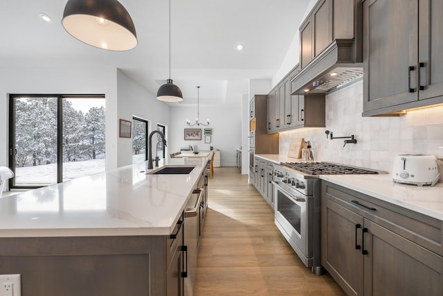 kitchen with light stone countertops, sink, high end range, and pendant lighting