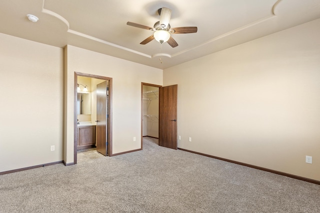 unfurnished bedroom with a spacious closet, ceiling fan, ensuite bathroom, light carpet, and a closet