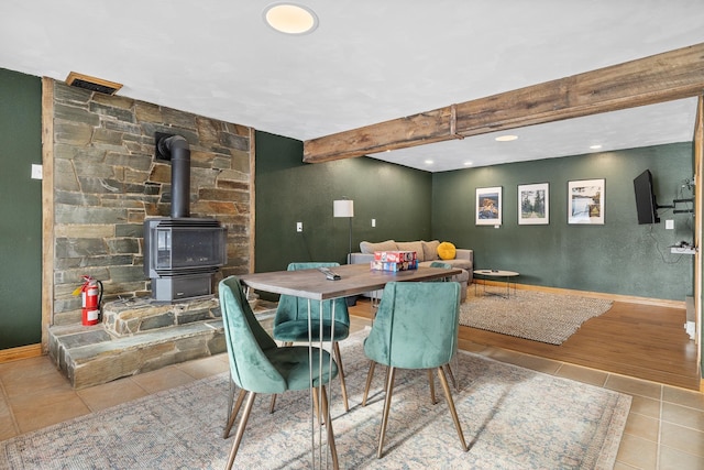 dining room with a wood stove, beamed ceiling, and light tile patterned flooring