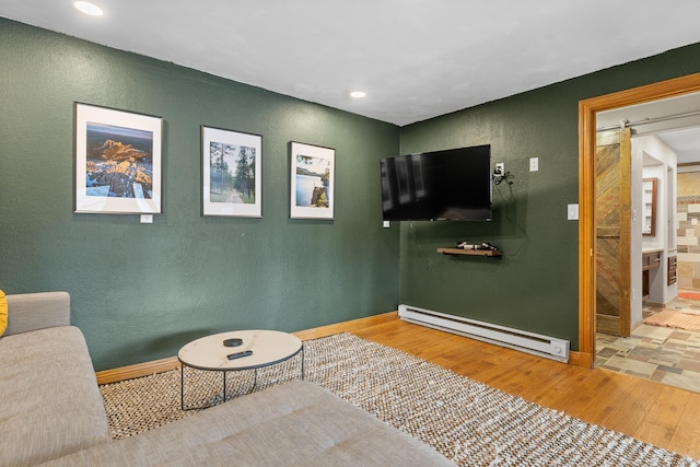 living area with a barn door, hardwood / wood-style flooring, and baseboard heating