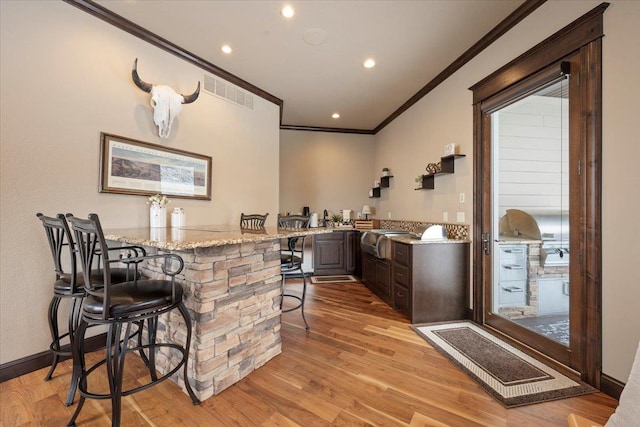 bar featuring light stone countertops, ornamental molding, dark brown cabinetry, and light hardwood / wood-style flooring