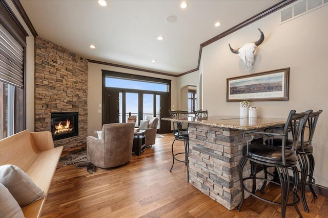 bar with light stone counters, a fireplace, hardwood / wood-style flooring, and ornamental molding