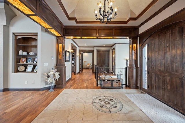 entryway with light hardwood / wood-style floors, an inviting chandelier, crown molding, and ornate columns