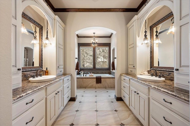 bathroom with tiled tub, vanity, a notable chandelier, and ornamental molding