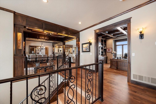 corridor featuring coffered ceiling, an inviting chandelier, ornamental molding, beamed ceiling, and wood-type flooring