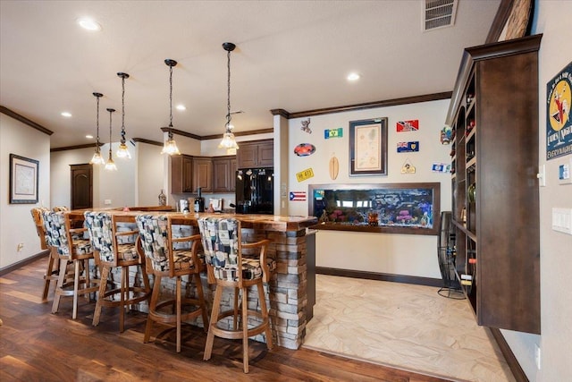 kitchen featuring a kitchen breakfast bar, black refrigerator, crown molding, hardwood / wood-style flooring, and dark brown cabinets