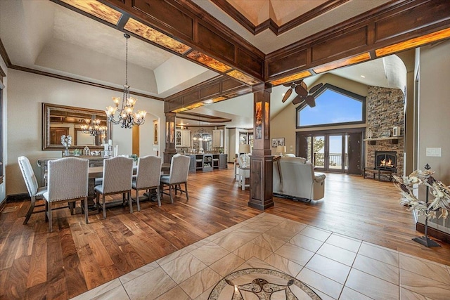 dining space with hardwood / wood-style floors, ceiling fan with notable chandelier, a stone fireplace, ornamental molding, and a towering ceiling