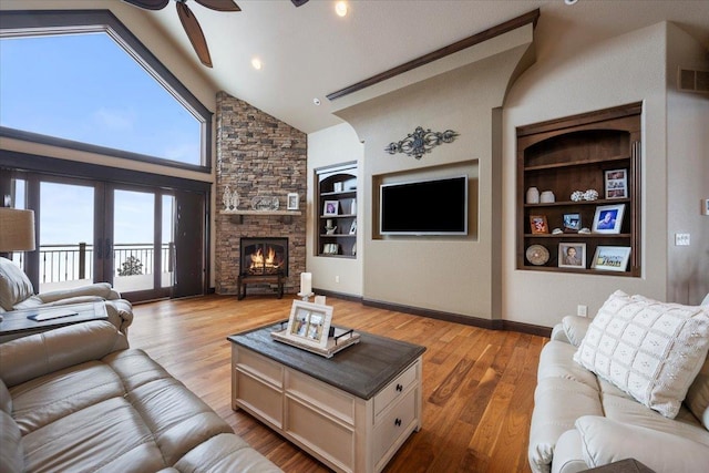 living room featuring built in shelves, ceiling fan, high vaulted ceiling, light hardwood / wood-style floors, and a fireplace