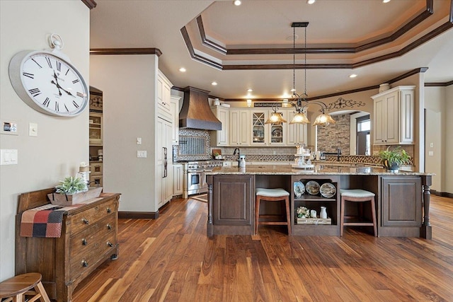 kitchen with crown molding, decorative backsplash, high end stove, an island with sink, and custom range hood