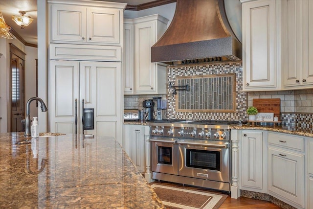 kitchen with stone counters, custom range hood, premium appliances, and white cabinetry