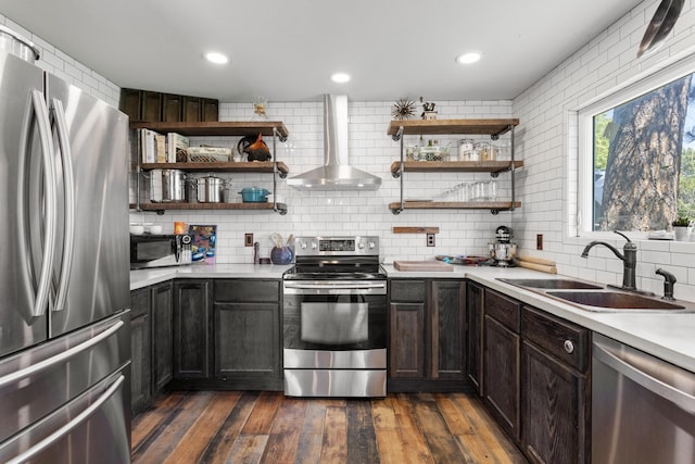 kitchen with backsplash, dark wood-type flooring, wall chimney range hood, sink, and stainless steel appliances