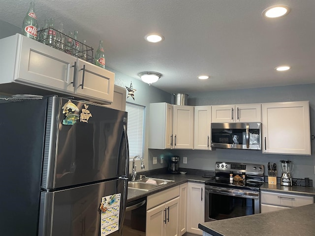 kitchen with appliances with stainless steel finishes, a textured ceiling, white cabinetry, and sink