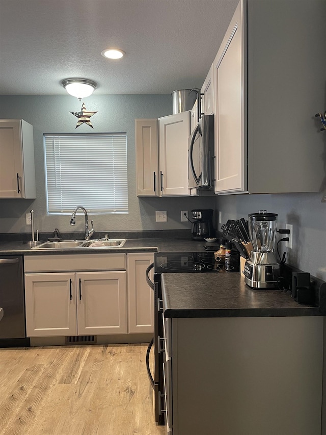 kitchen with white cabinetry, sink, stainless steel appliances, a textured ceiling, and light wood-type flooring