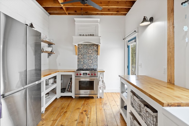 kitchen featuring butcher block countertops, light wood-style floors, appliances with stainless steel finishes, open shelves, and beamed ceiling