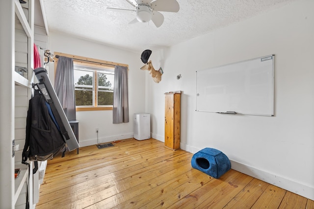 interior space featuring wood-type flooring, ceiling fan, a textured ceiling, and baseboards