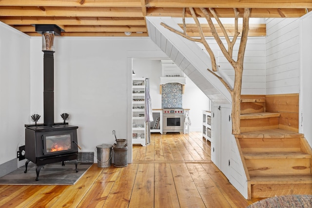 interior space with hardwood / wood-style flooring, wood walls, a wood stove, and beamed ceiling