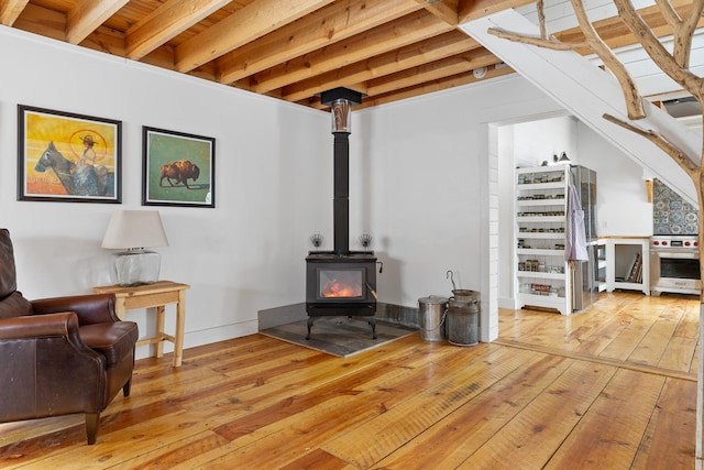 living area featuring hardwood / wood-style floors, beam ceiling, and a wood stove