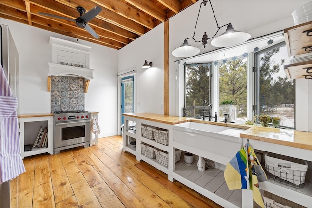 kitchen featuring hanging light fixtures, under cabinet range hood, light wood-style floors, wooden counters, and luxury stove