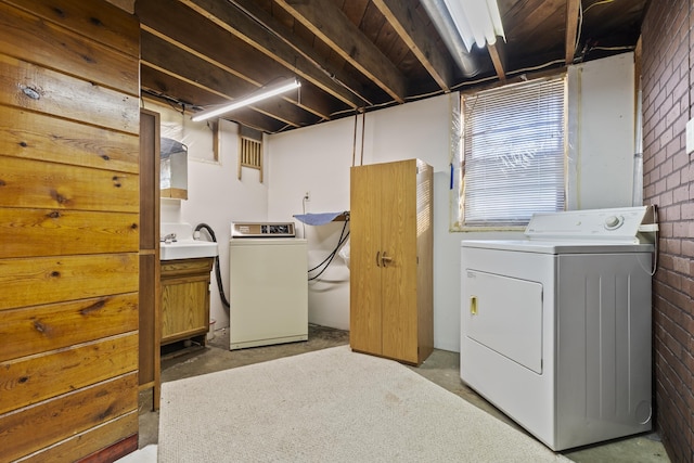 clothes washing area featuring independent washer and dryer, sink, and brick wall