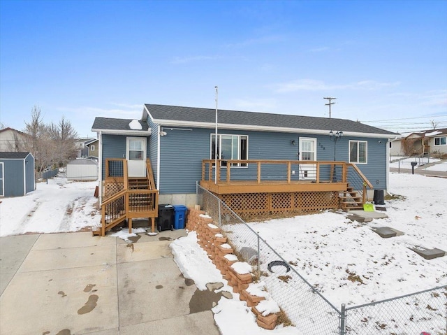 snow covered back of property with a deck and a storage shed