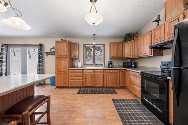 kitchen featuring light hardwood / wood-style floors, a wealth of natural light, black appliances, and pendant lighting