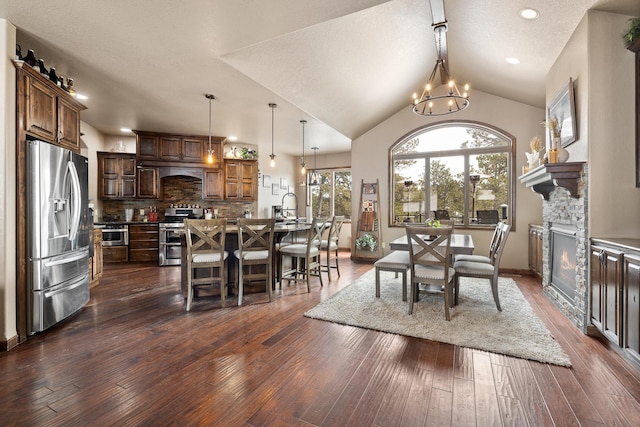 dining room featuring dark hardwood / wood-style flooring, lofted ceiling, an inviting chandelier, and a fireplace