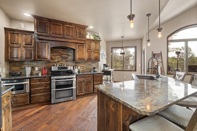 kitchen with pendant lighting, sink, a kitchen island with sink, backsplash, and stainless steel appliances