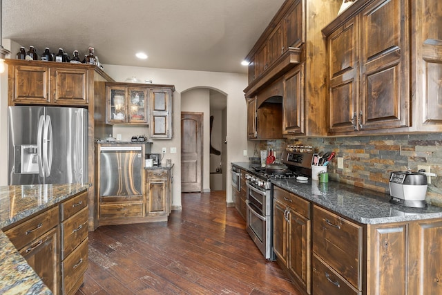 kitchen featuring stainless steel appliances, dark stone countertops, backsplash, and dark hardwood / wood-style flooring