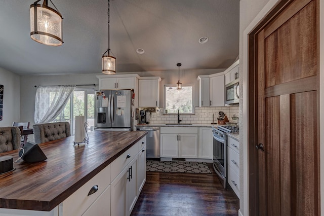 kitchen featuring white cabinetry, butcher block countertops, stainless steel appliances, hanging light fixtures, and sink