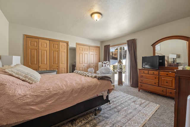 bedroom featuring a textured ceiling, light carpet, and multiple closets