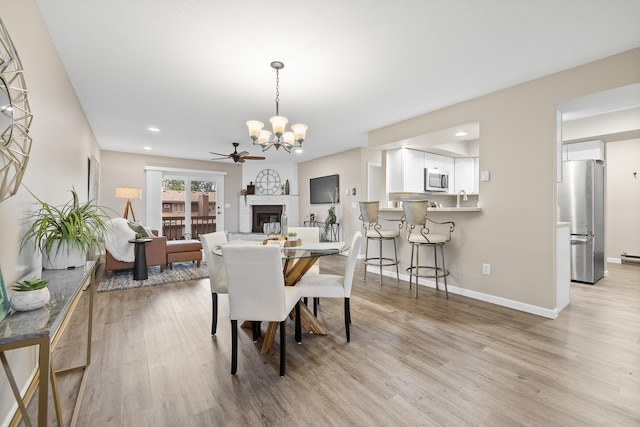 dining space featuring ceiling fan with notable chandelier, light hardwood / wood-style flooring, and a fireplace