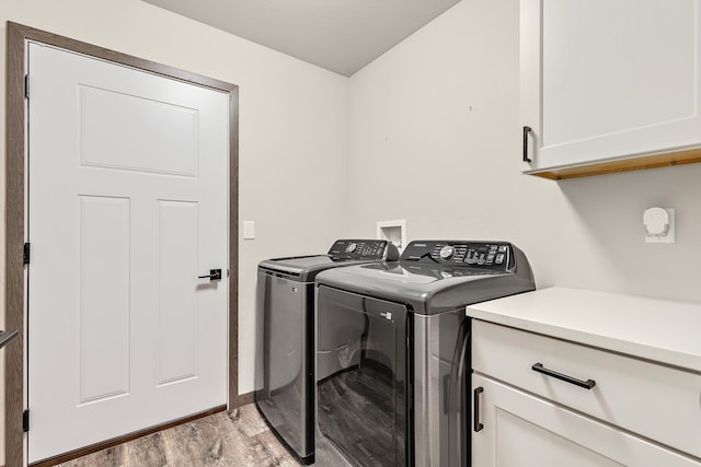 clothes washing area featuring cabinets, light hardwood / wood-style flooring, and washing machine and clothes dryer