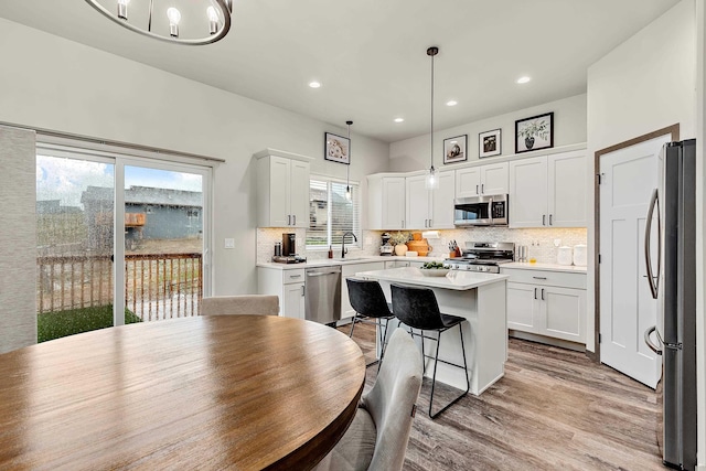 kitchen featuring appliances with stainless steel finishes, white cabinetry, a kitchen island, and decorative light fixtures